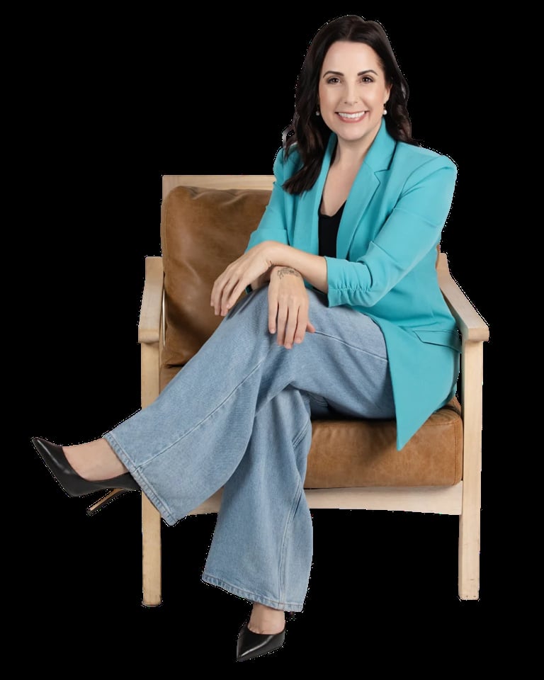 Professional woman with dark hair sitting in a tan leather chair, wearing a turquoise blazer and jeans, smiling at camera