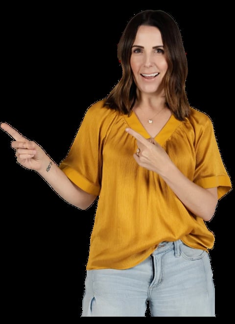 Woman in mustard yellow v-neck shirt and light jeans smiling and pointing to the right against a black background